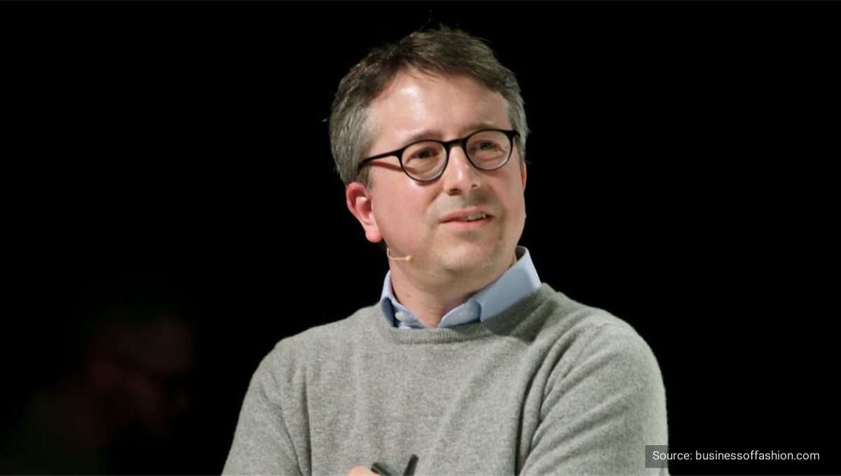 A man in glasses and a grey jumper speaking on a darkened conference stage.