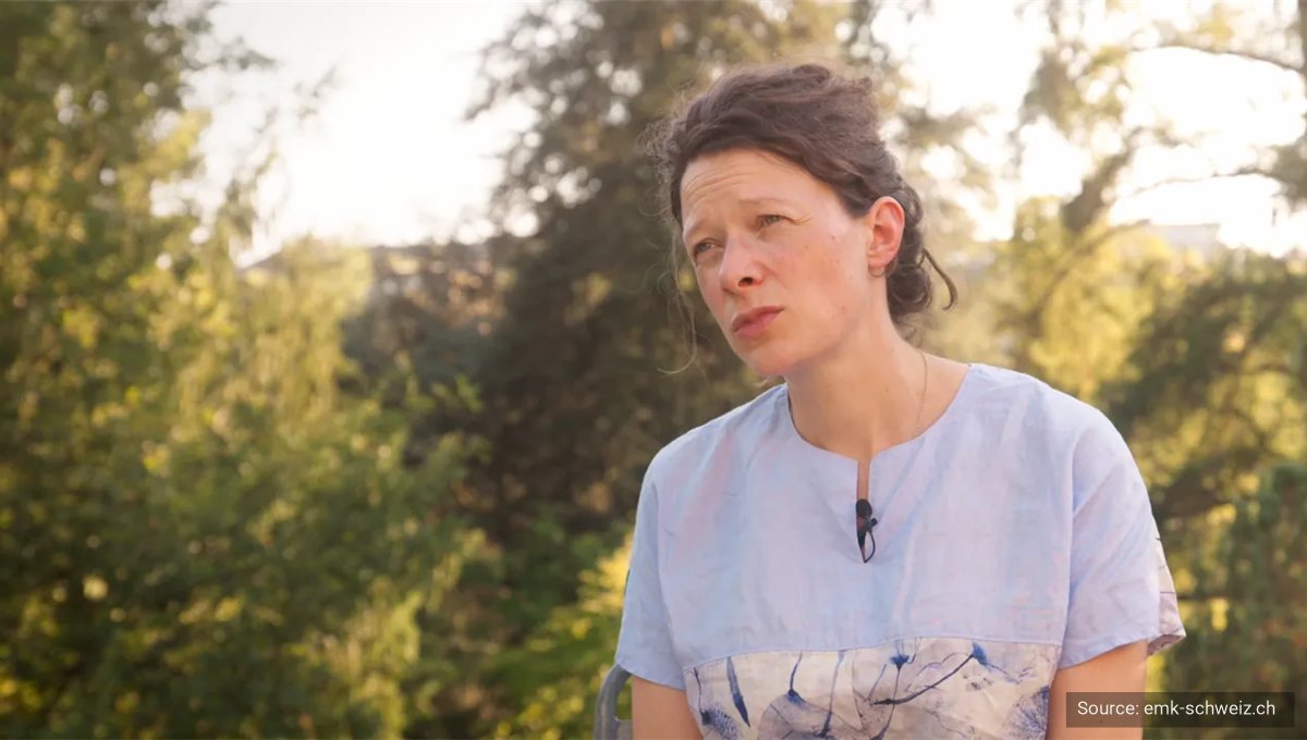 A woman being interviewed outdoors among trees in low evening light.