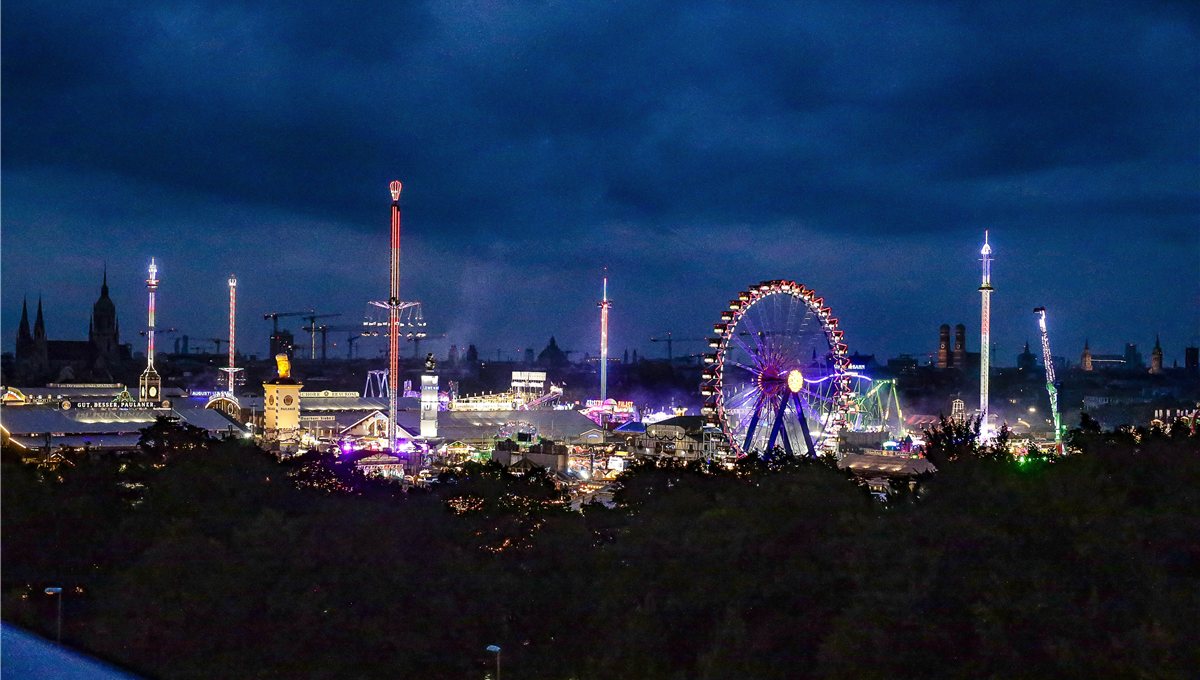 The Oktoberfest fairground at dusk, the big wheel and drop tower lit against a dark Munich skyline.