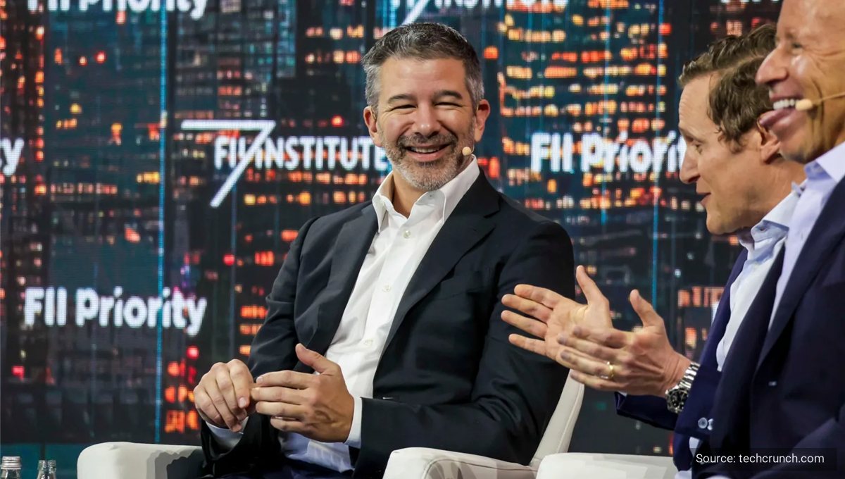 Travis Kalanick talking and gesturing on stage against a lit city backdrop.
