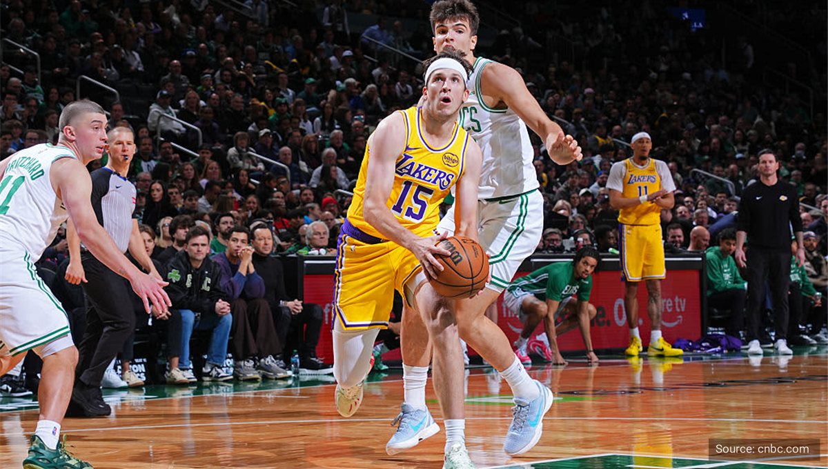 A Lakers player driving to the basket past a Celtics defender in a packed arena.