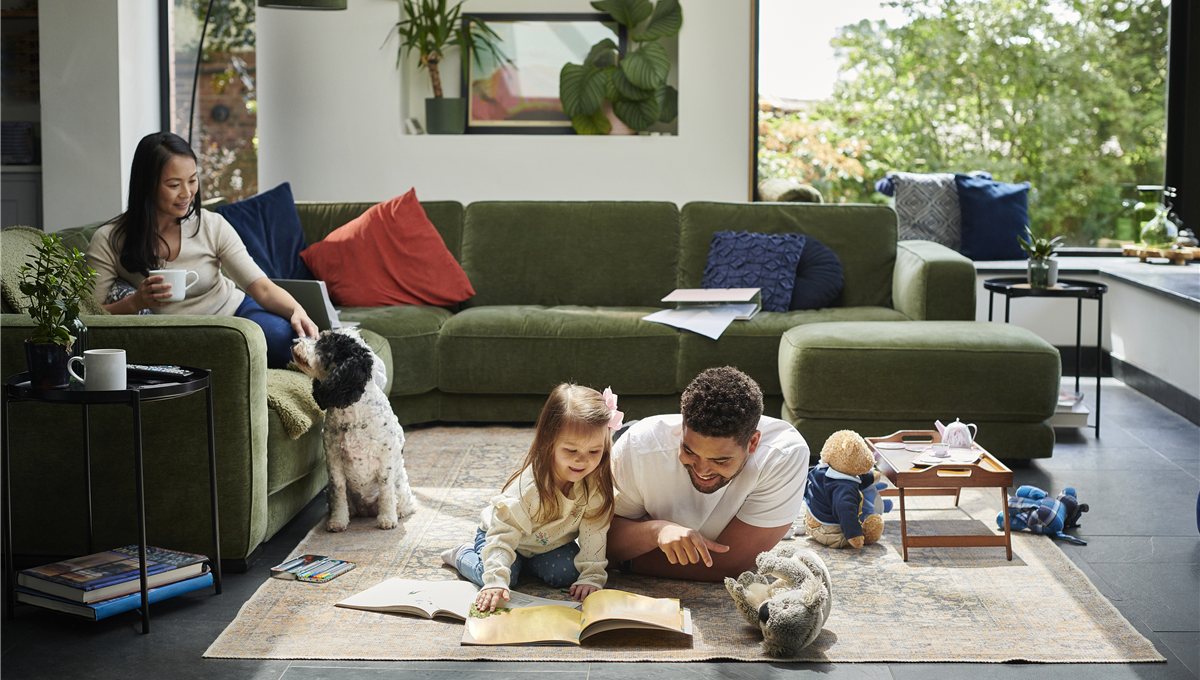 A family reading a picture book on the floor of a living room, with a dog beside them.