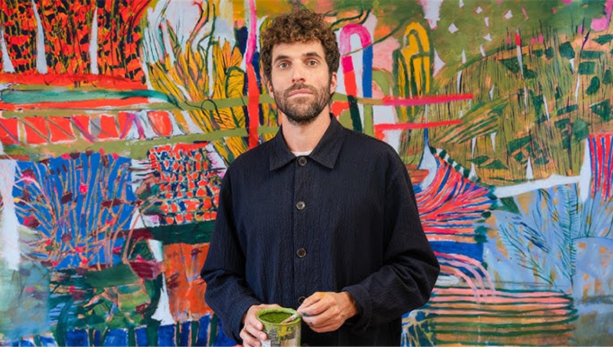 A man holding a matcha in front of a large, brightly painted canvas.
