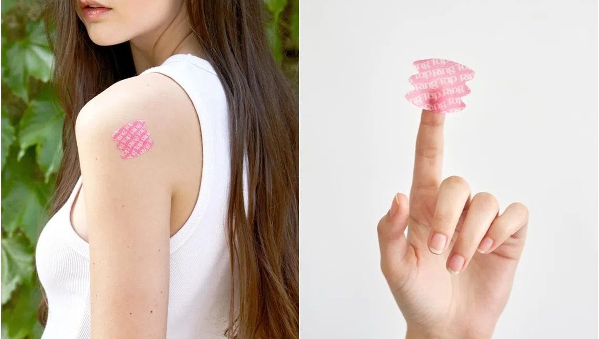 A pink nutrition patch worn on an upper arm, and a fingertip holding another one.