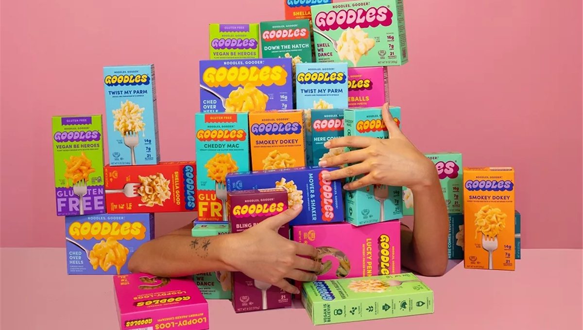Stacked boxes of Goodles macaroni in bright colours, with hands reaching into the pile.