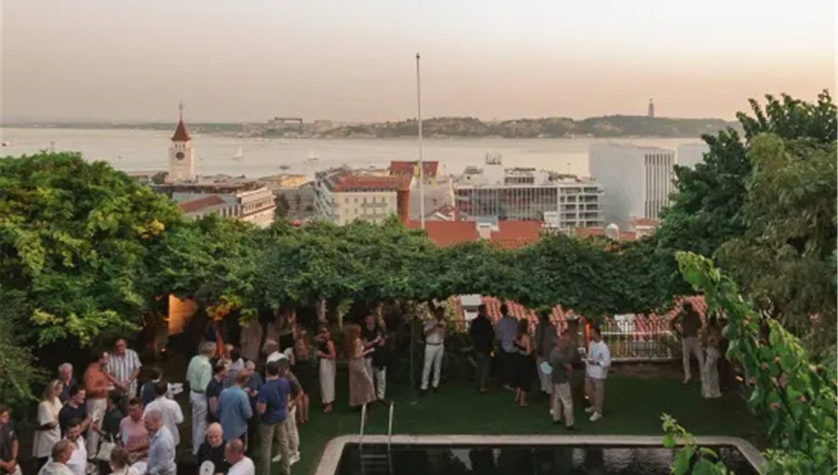 A rooftop reception with guests talking, above the rooftops of Lisbon and the Tagus.