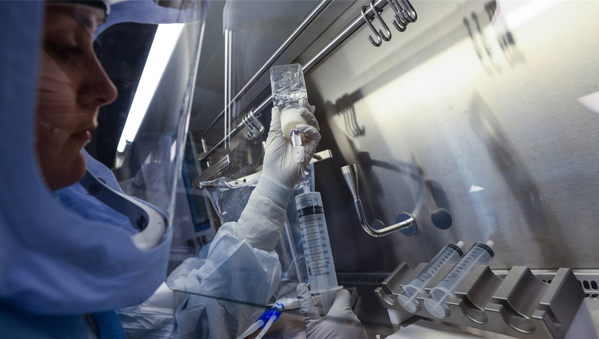 A researcher in a protective suit working at a sterile pharmaceutical isolator.