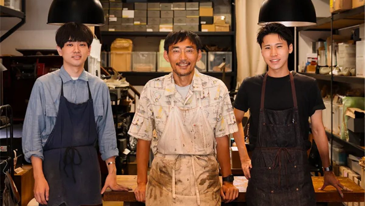 Three shoemakers in aprons standing in their Tokyo workshop.